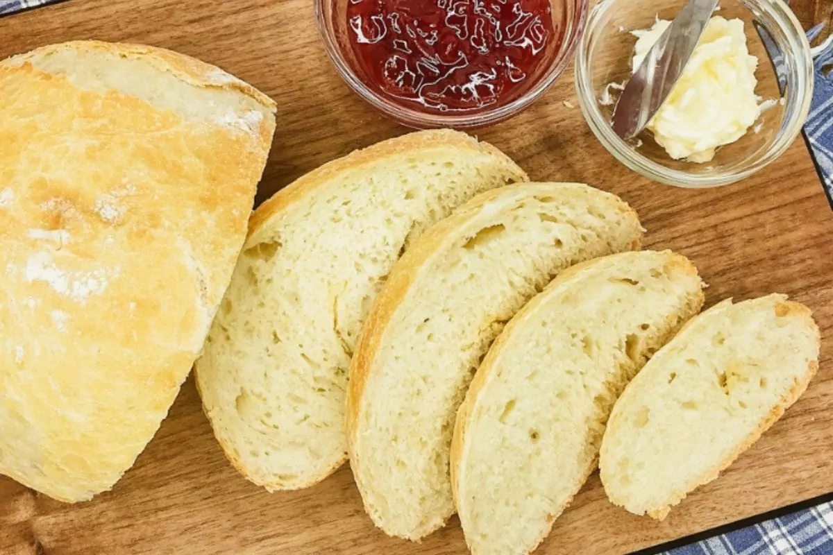 sliced bread on cutting board with bowl of jam and butter.