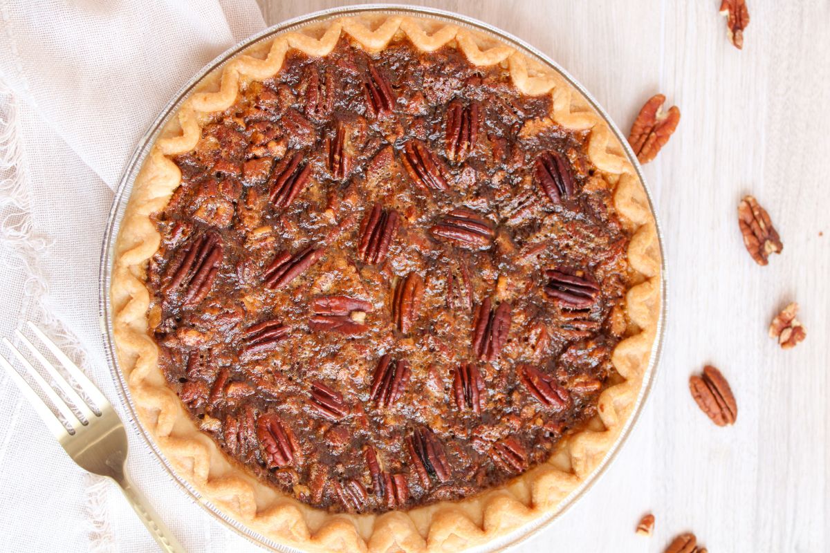 whole pecan pie with pecan scattered around and a fork next to it