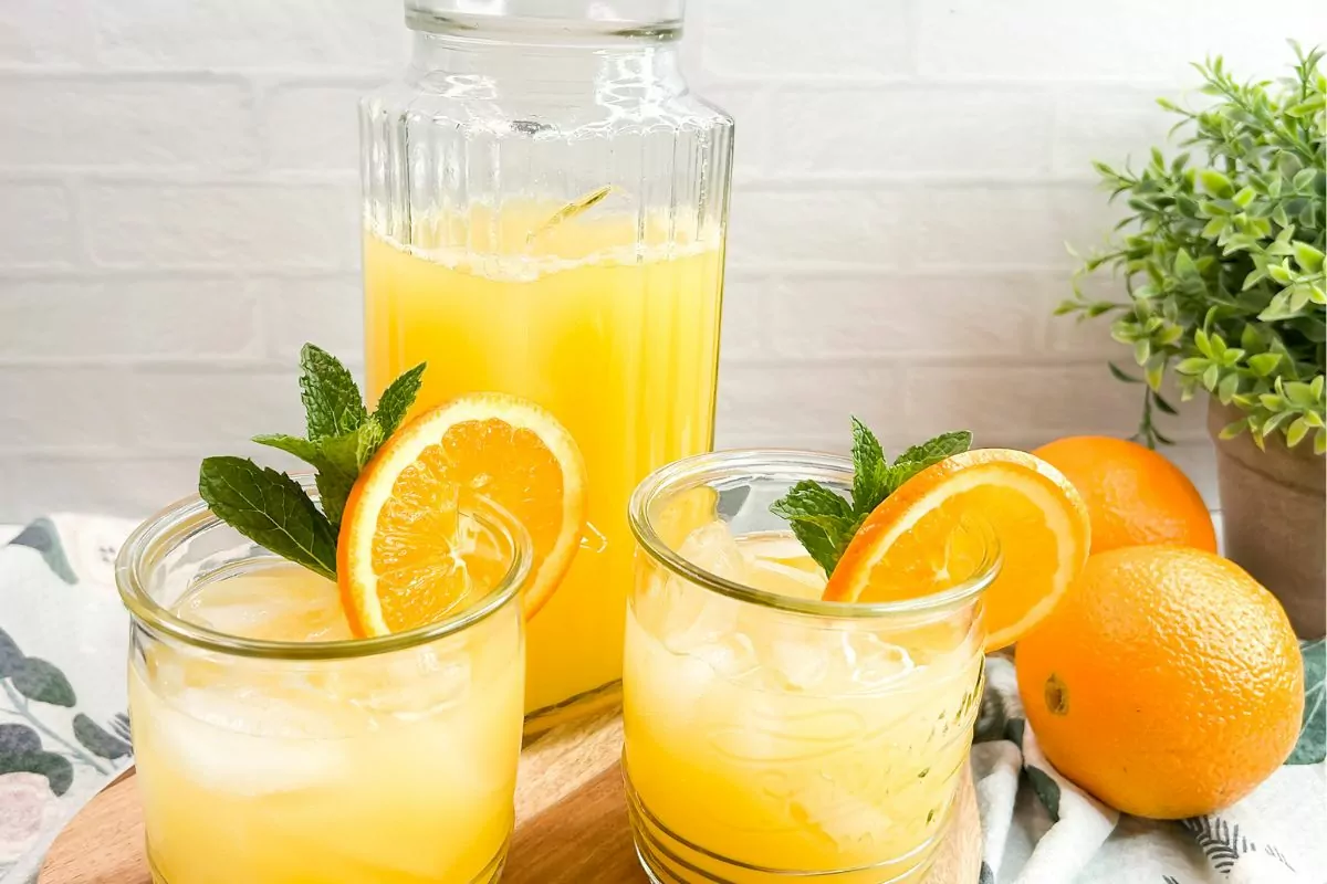 A refreshing Pineapple Orange Spritzer in a glass pitcher, garnished with orange slices and fresh mint.