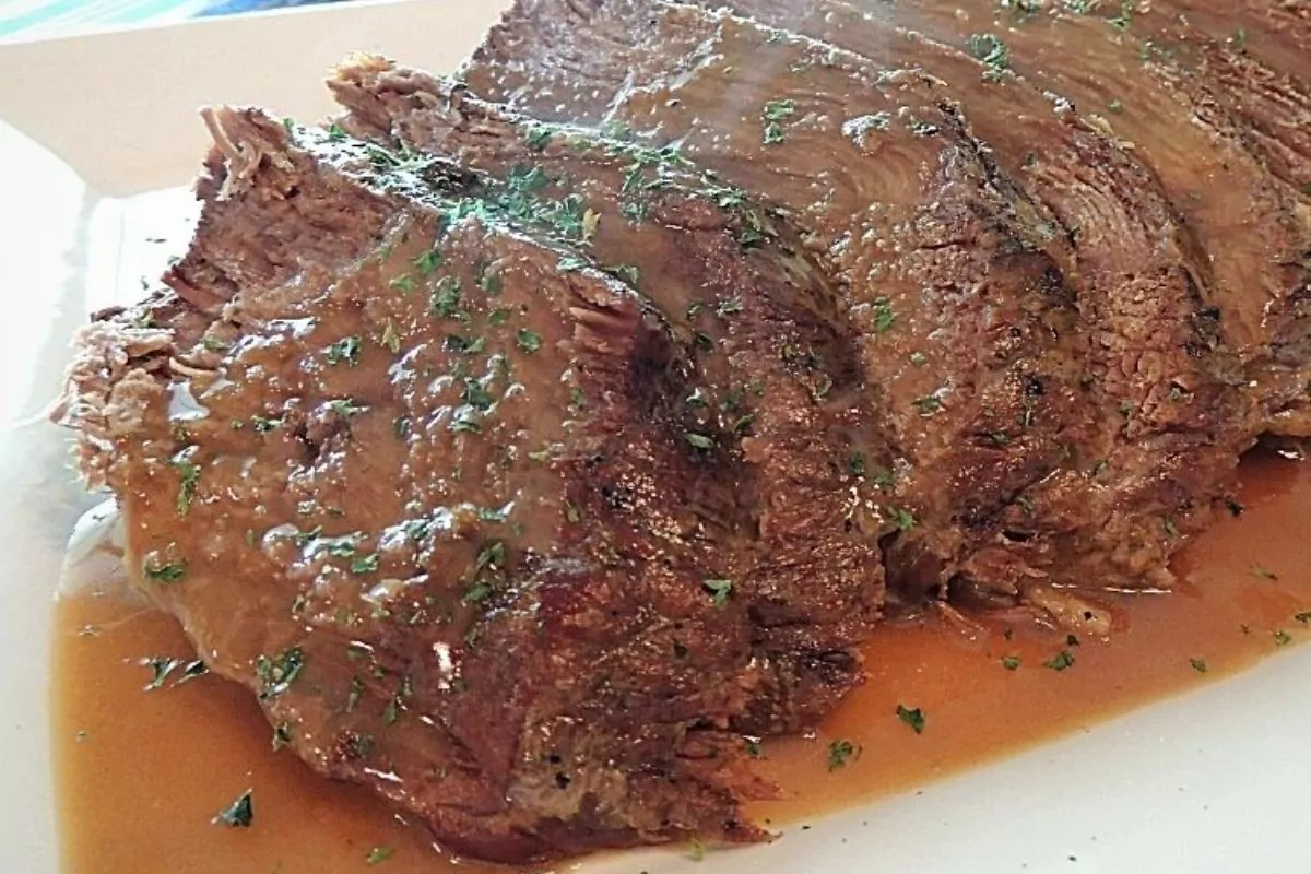 slices of tender pot roast with gravy on white tray.