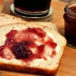 homemade bread sliced on cutting board with butter and jam.