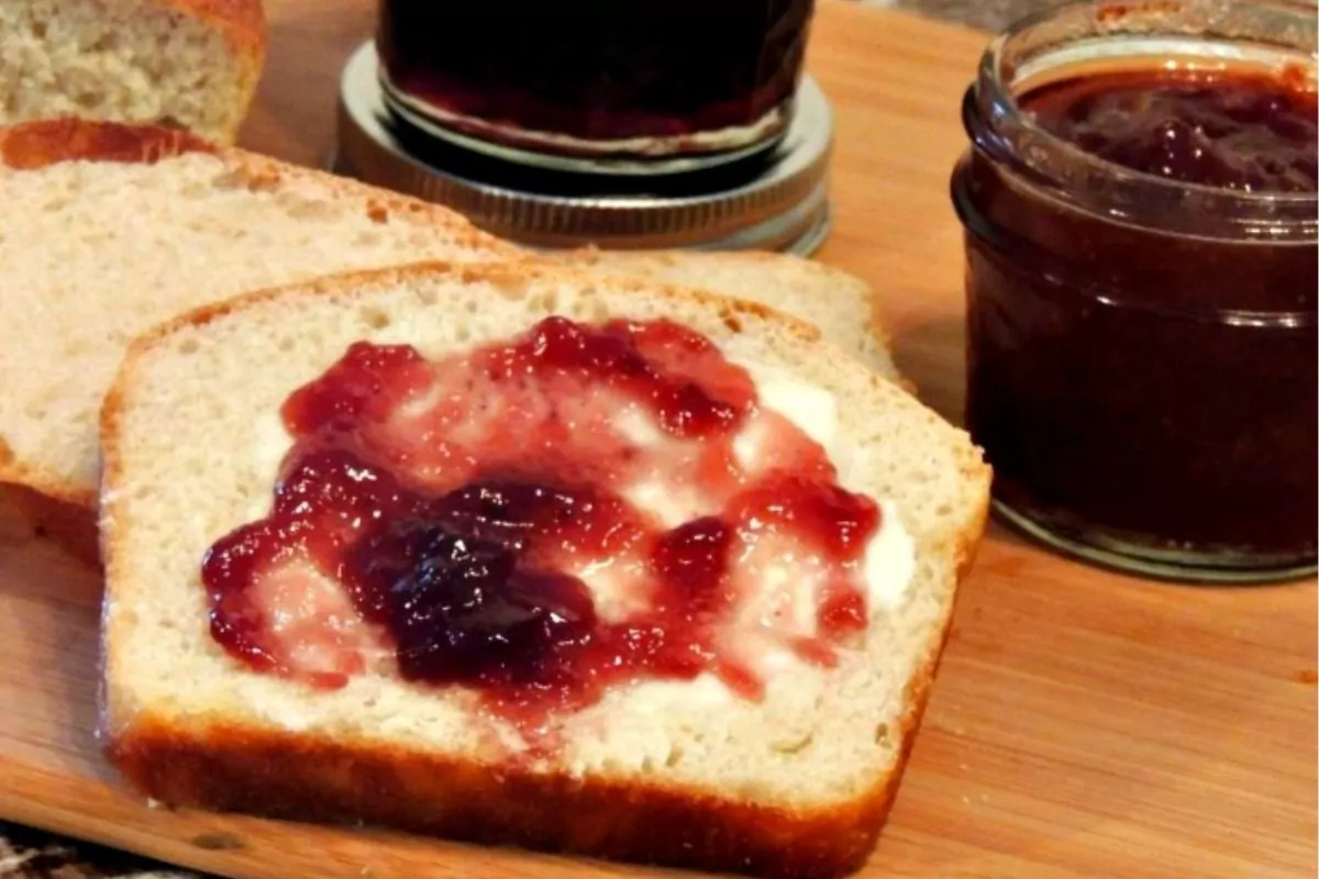 homemade bread sliced on cutting board with butter and jam.