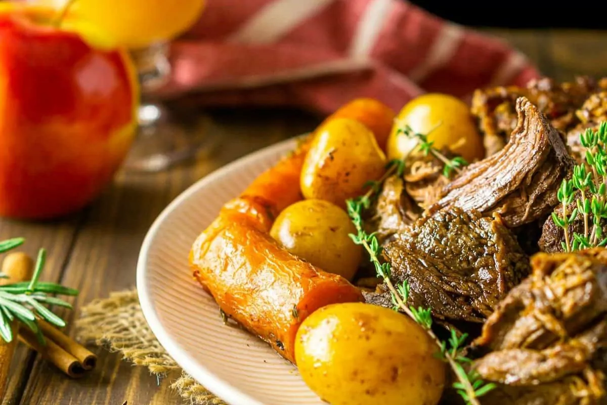 a plate of beef chuck with potatoes, carrots and gravy