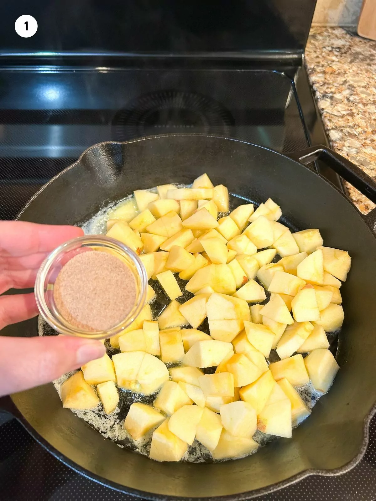 chopped apples cooking in skillet with small bowl of cinnamon sugar on top.