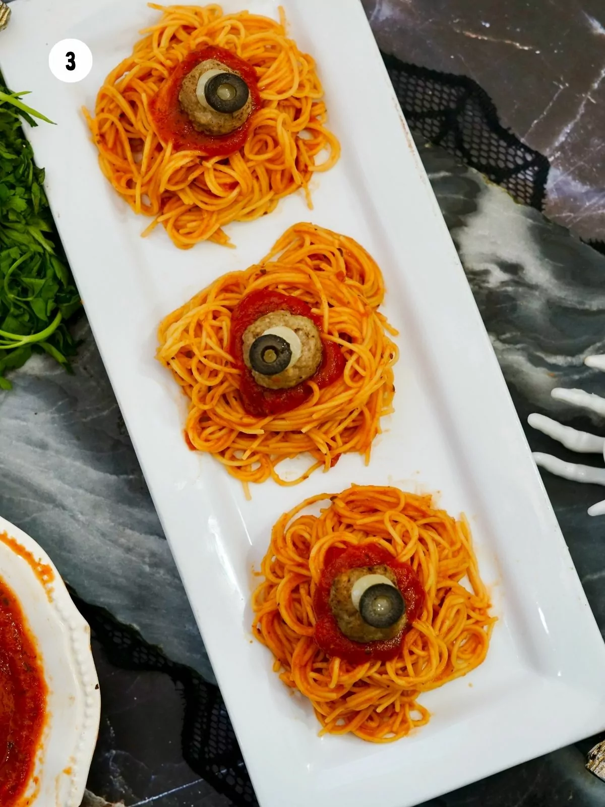 closeup of meatballs with piece of cheese and olive on top of spaghetti with sauce.