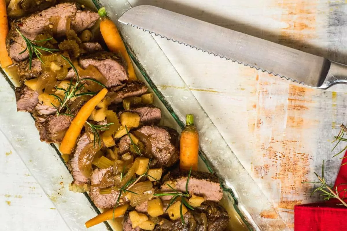 a plate of beef with carrots potato and rosemary as toppings