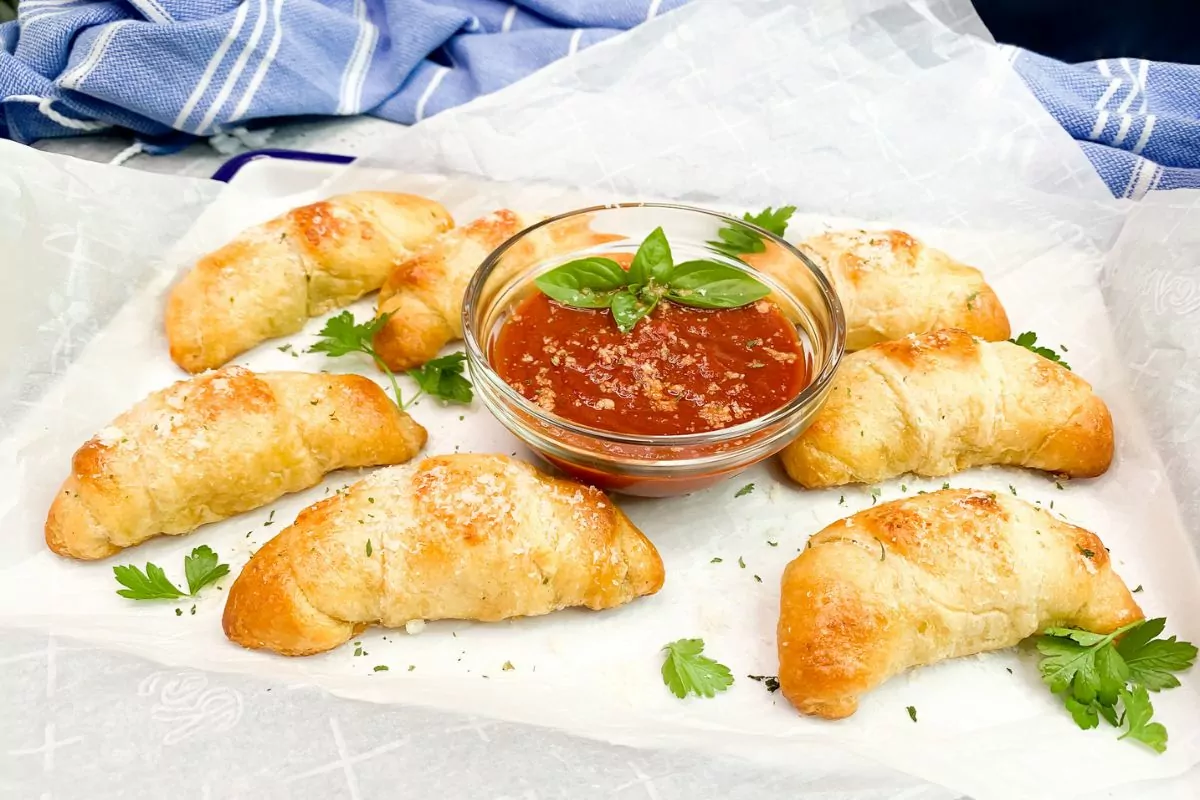 garlic butter crescents on plate with small bowl of tomato sauce for dipping in the center.