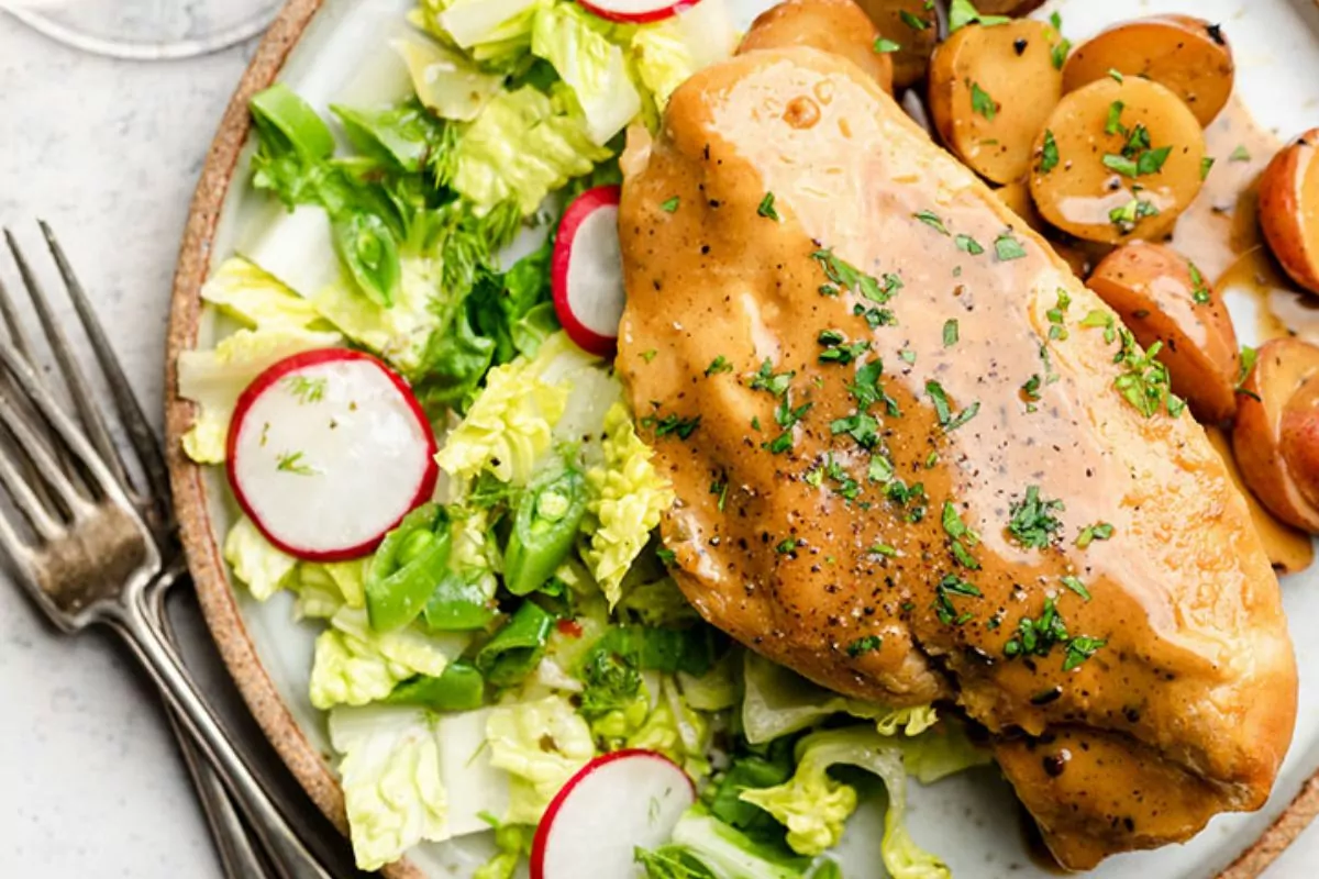 a plate of juicy cooked chicken breast with cabbage potato and red onion