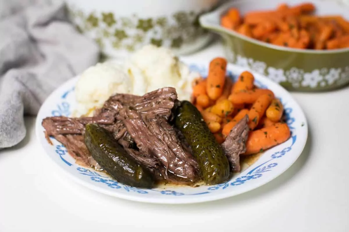 a plate of beef with mashed potato carrots and pickles