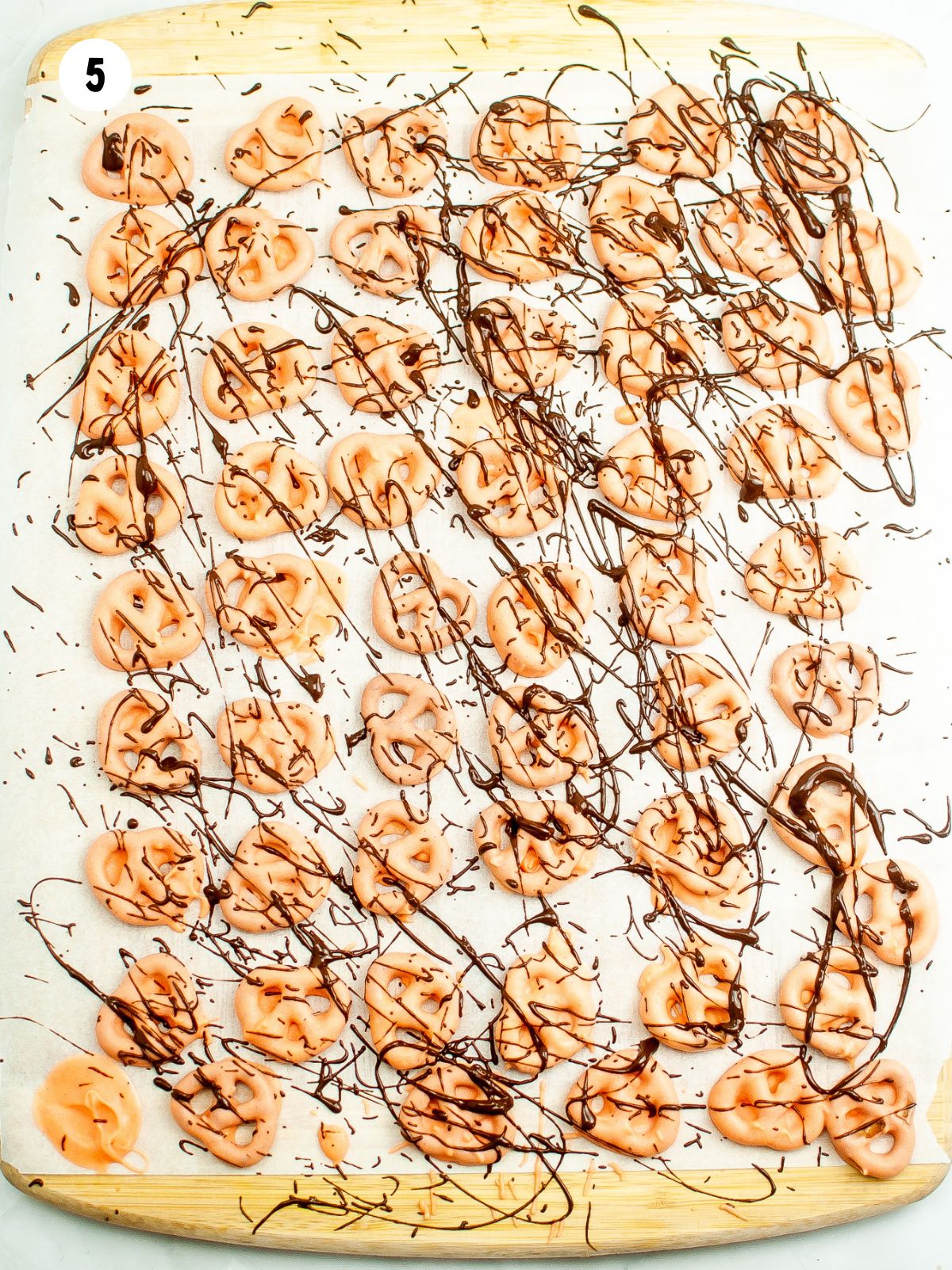 pretzels dipped in orange chocolate on parchment paper with melted chocolate drizzled on top.