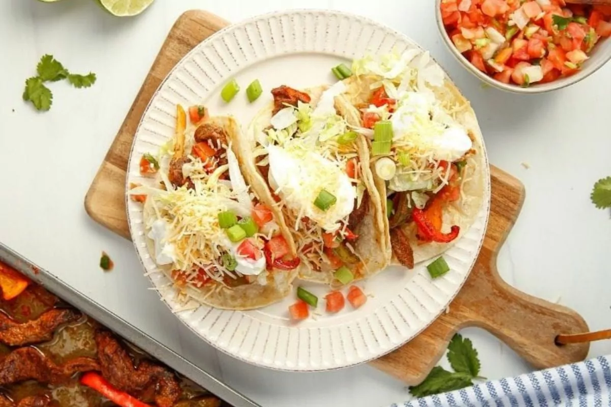 Steak chunks and veggies bake on a sheet pan with sauces, cheeses and taco toppings