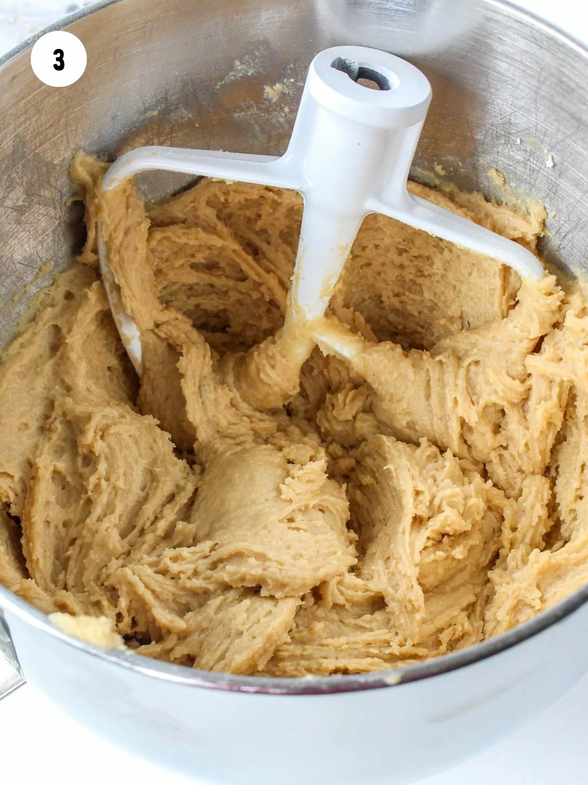 cookie dough in a stainless steel mixing bowl with the paddle attachment in the dough