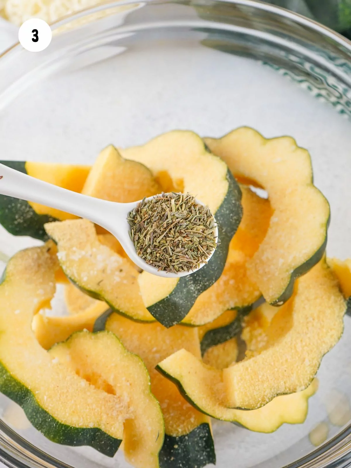 teaspoon of herbs de provence over a bowl of sliced acorn squash