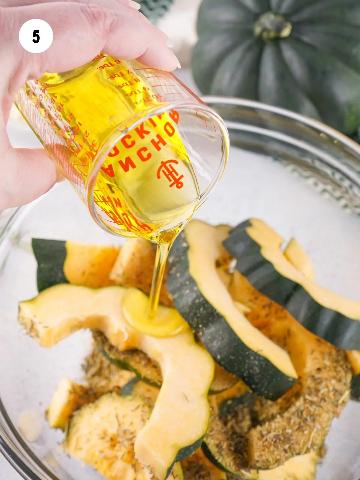 olive oil pouring over the seasoned acorn squash