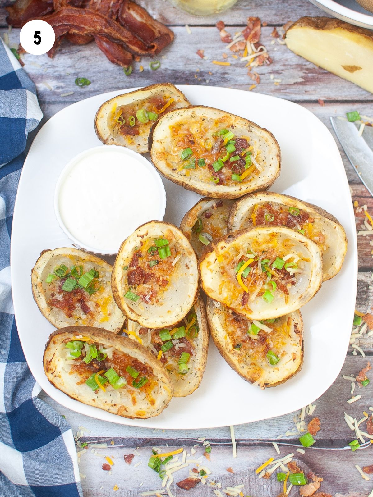 potato skins garnished with green onions served on a white platter with a bowl of ranch dip