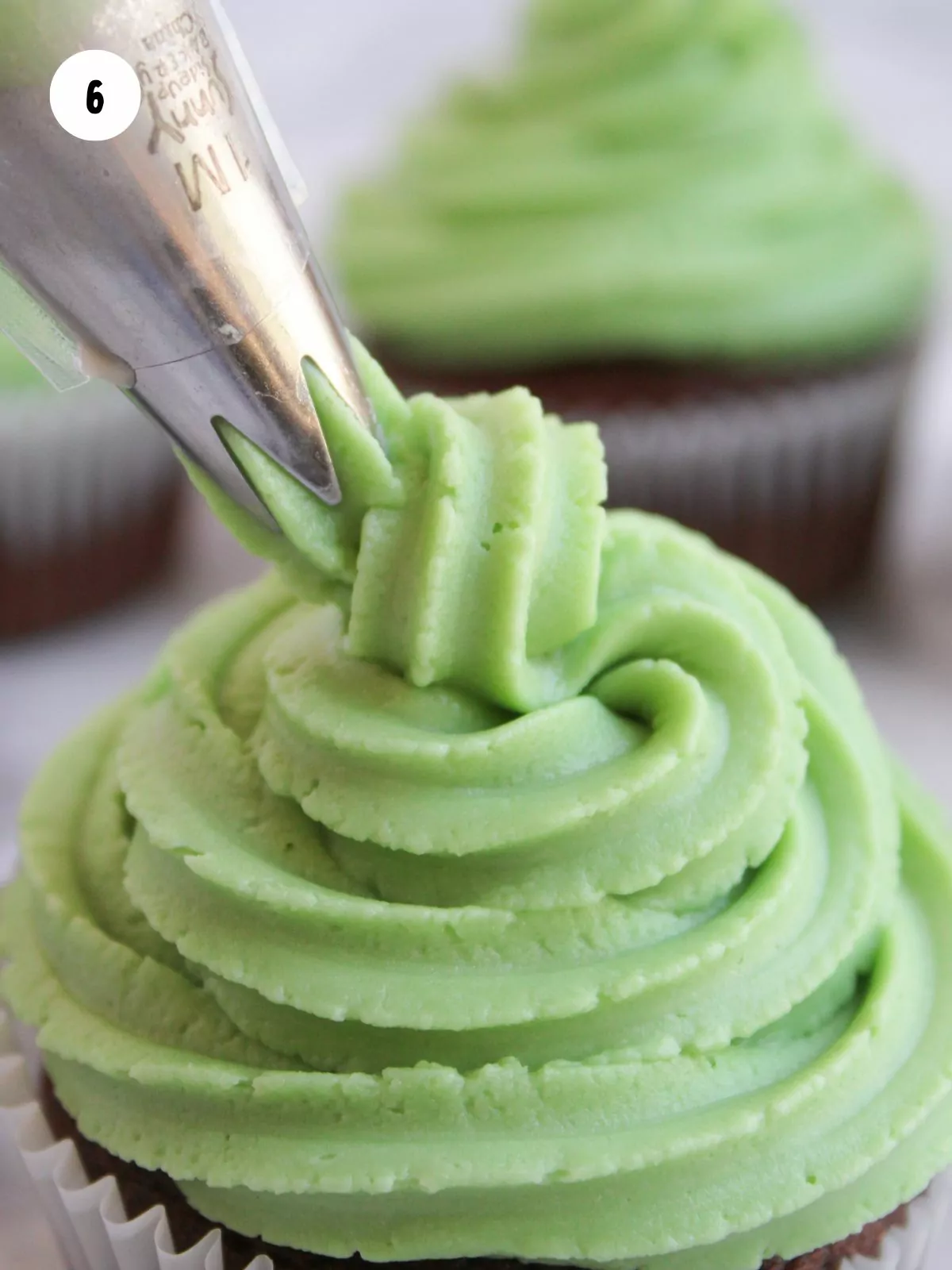 green frosting being piped in a swirl on top of a cupcake