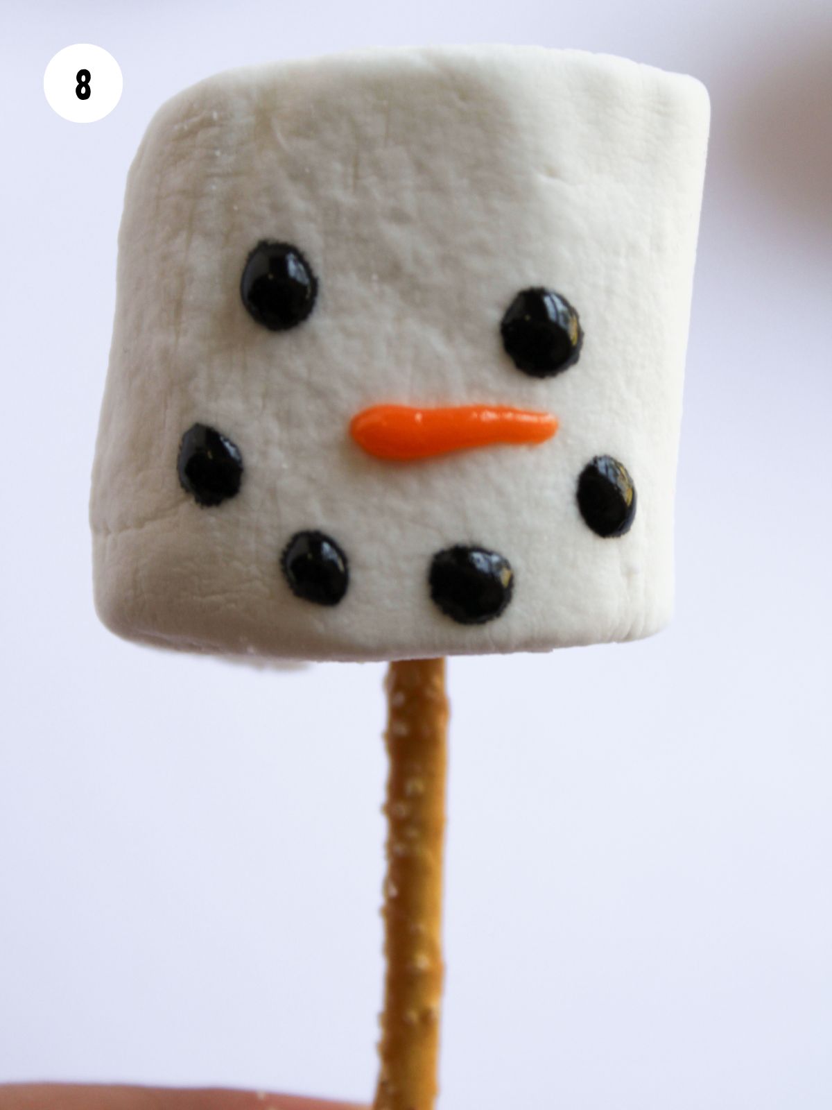 Marshmallow with a snowman face stuck on a pretzel stick