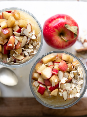 overnight oats with apples in mason jars with cinnamon sticks and two spoons.