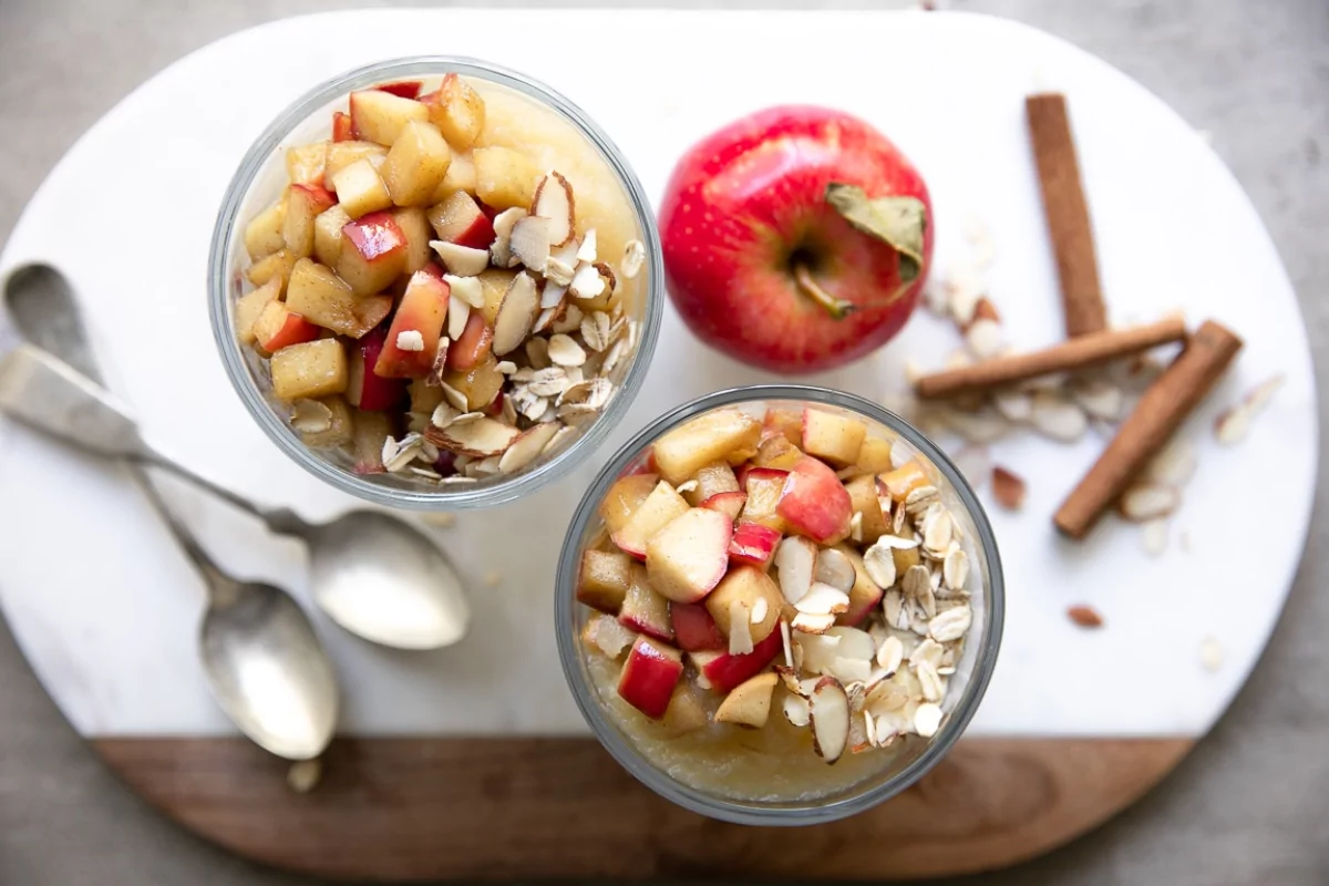 overnight oats with apples in mason jars with cinnamon sticks and two spoons.