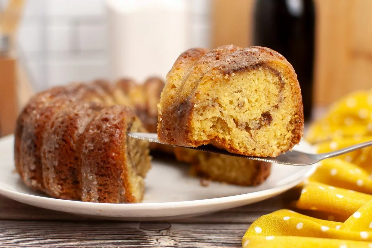slice of cinnamon streusel coffee cake on a serving knife with the rest of the bundt cake in the background