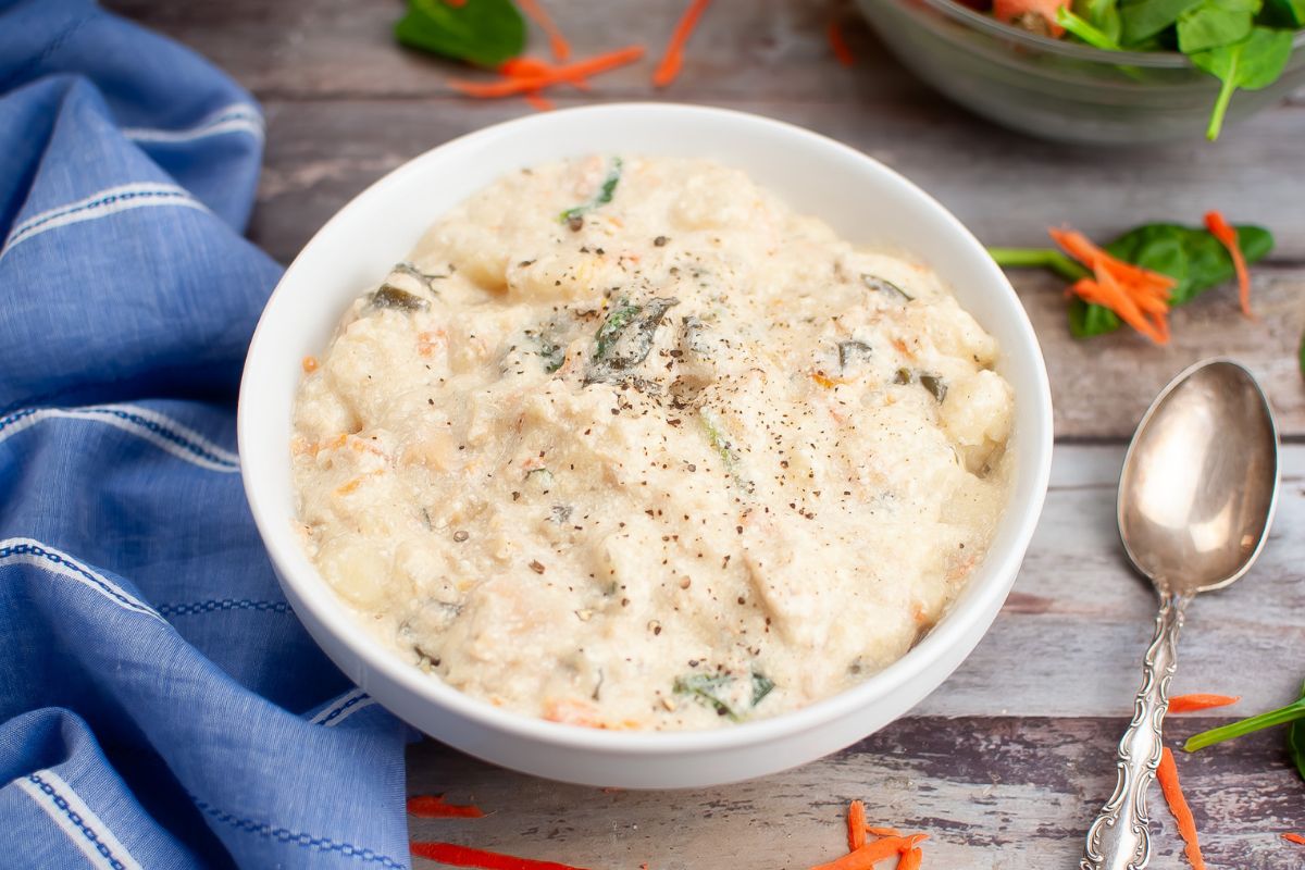 white bowl filled with chicken gnocchi soup with a spoon next to the bowl on the right and a blue kitchen towel on the left.