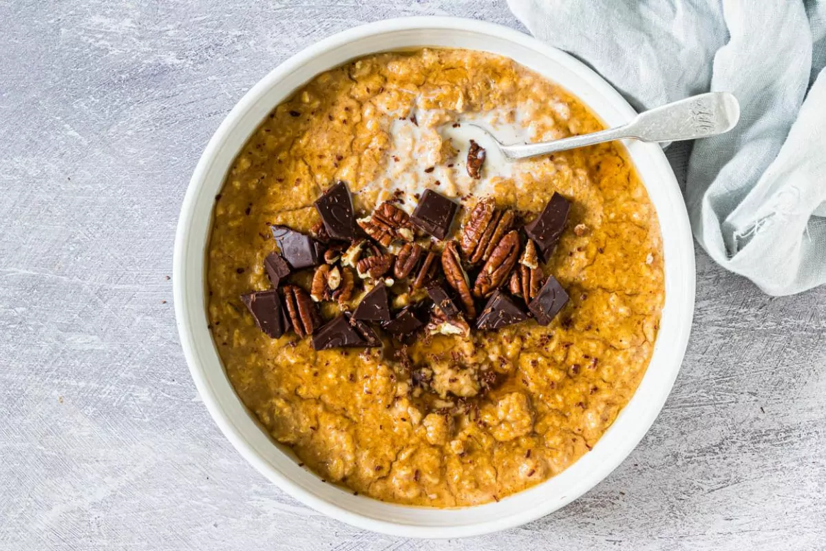 bowl of pumpkin oatmeal with pecans and chocolate chunks in white bowl with spoon.