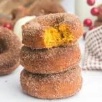 stack of 3 pumpkin donuts with the top one with a bite taken out showing the orange inside.