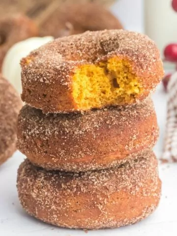 stack of 3 pumpkin donuts with the top one with a bite taken out showing the orange inside.