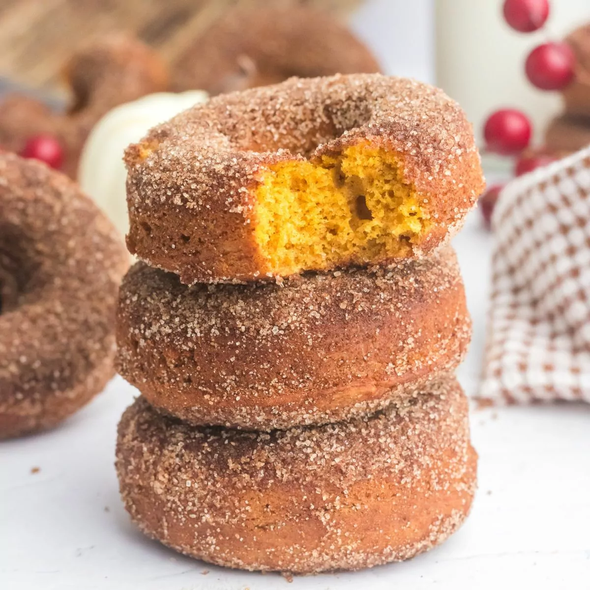 stack of 3 pumpkin donuts with the top one with a bite taken out showing the orange inside.