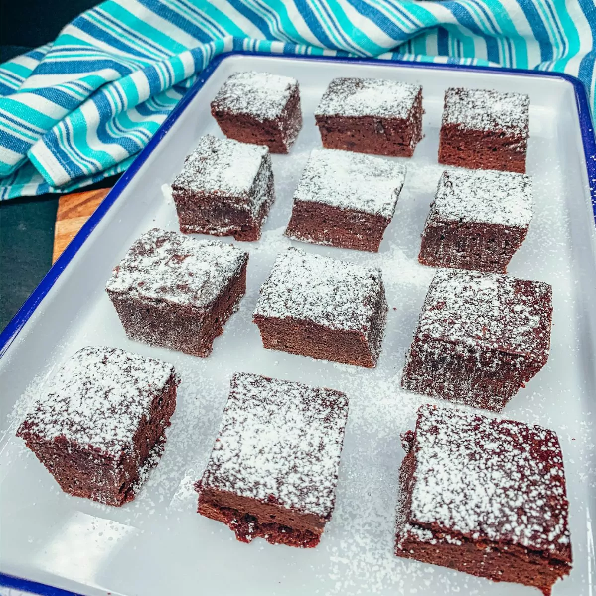 brownies sliced into squares with powdered sugar on white tray.