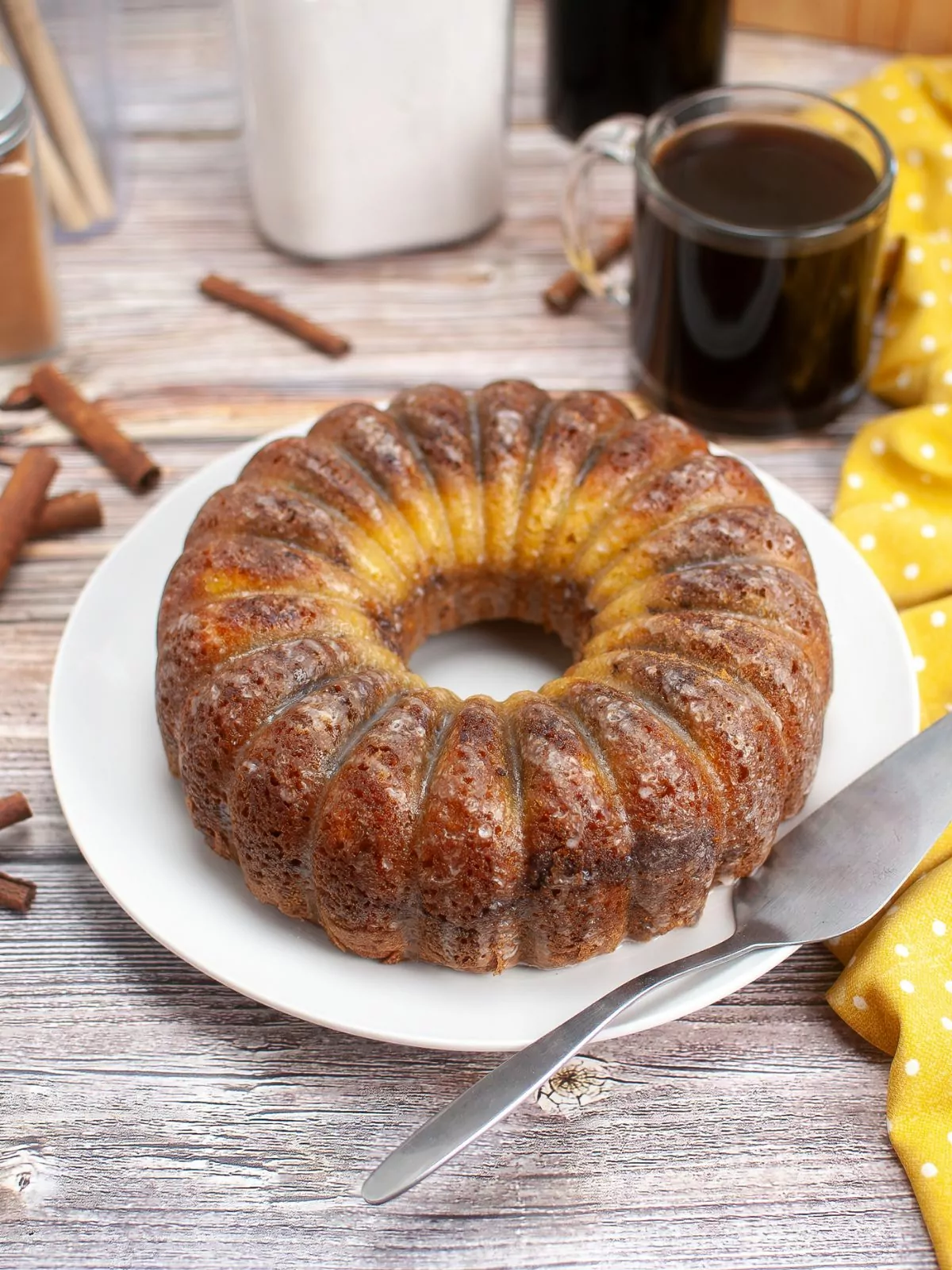 bundt cake of Cinnamon Streusel Coffee Cake on a white platter. A cup of coffee in the background