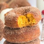 stack of 3 pumpkin donuts with the top one with a bite taken out showing the orange inside with text