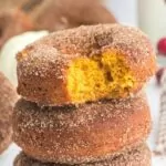 stack of 3 pumpkin donuts with the top one with a bite taken out showing the orange inside with text