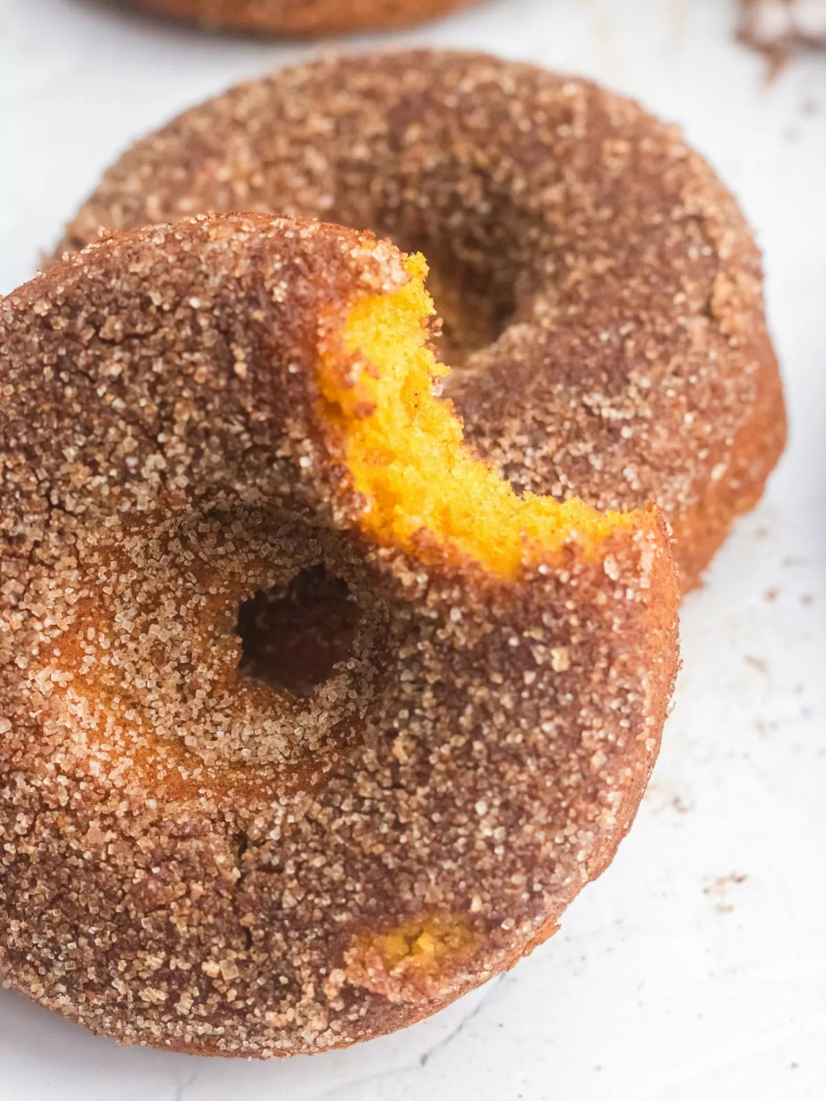 close up cinnamon sugar coated pumpkin donut with a bite taken out