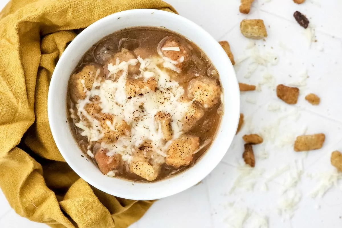 bowl of French Onion Soup with croutons and cheese on yellow towel.