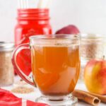 glass of prepared apple cider with fresh apples in background.