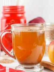 glass of prepared apple cider with fresh apples in background.