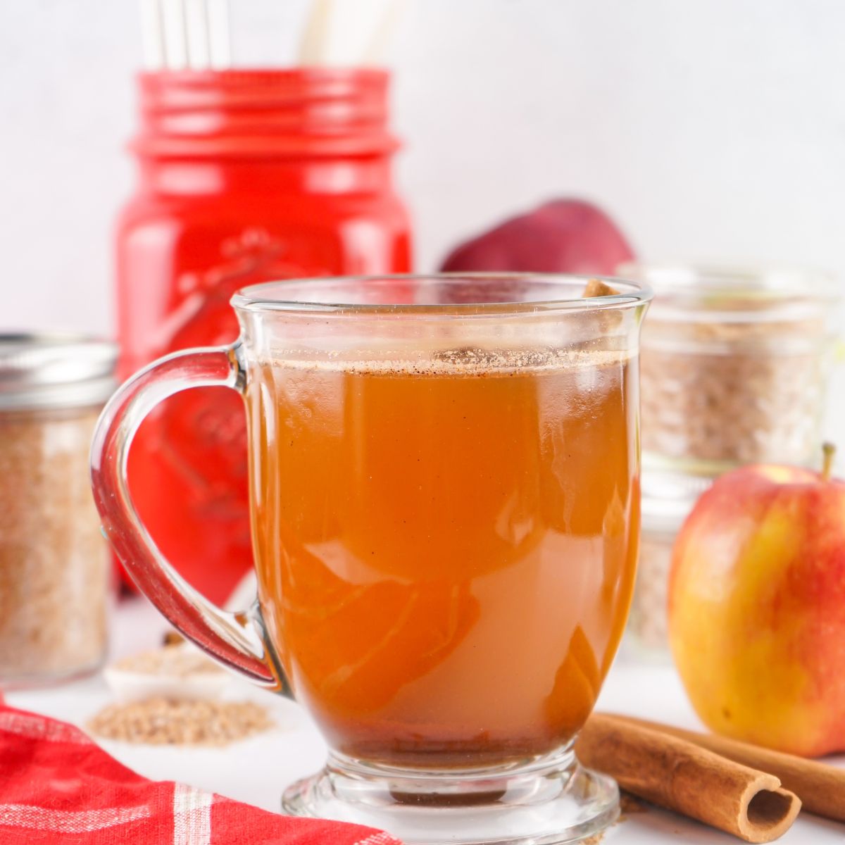 glass of prepared apple cider with fresh apples in background.