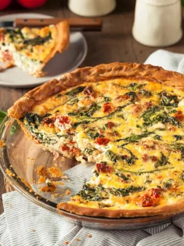 spinach bacon quiche in pie plate with slice missing.