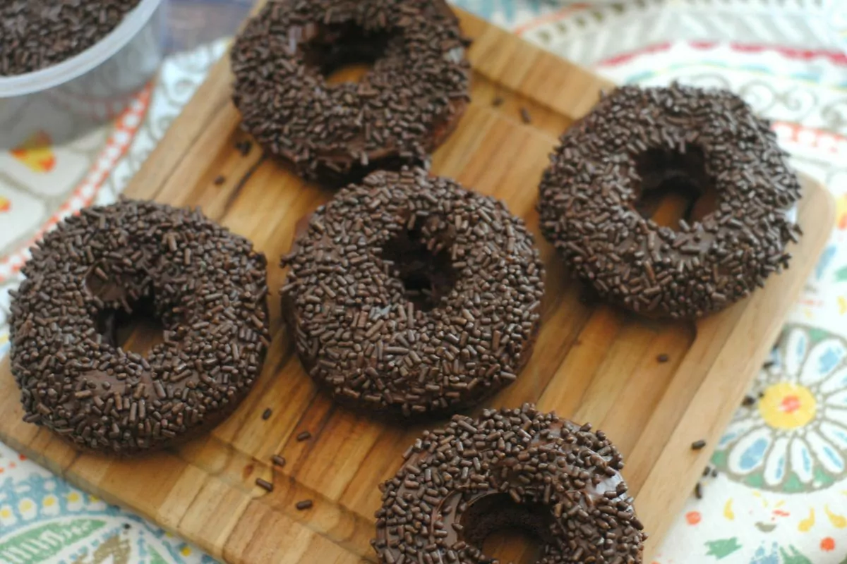 5 chocolate donuts with sprinkles on cutting board.