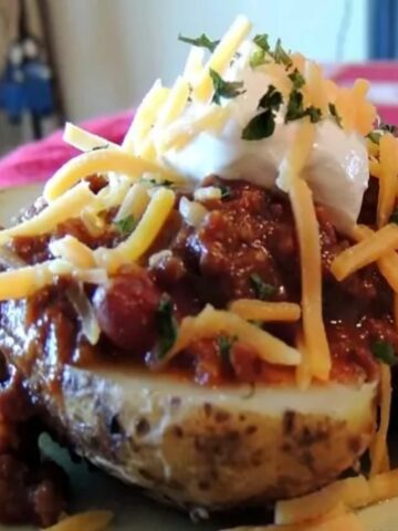 close up of chili on top of baked potato with cheese and sour cream.