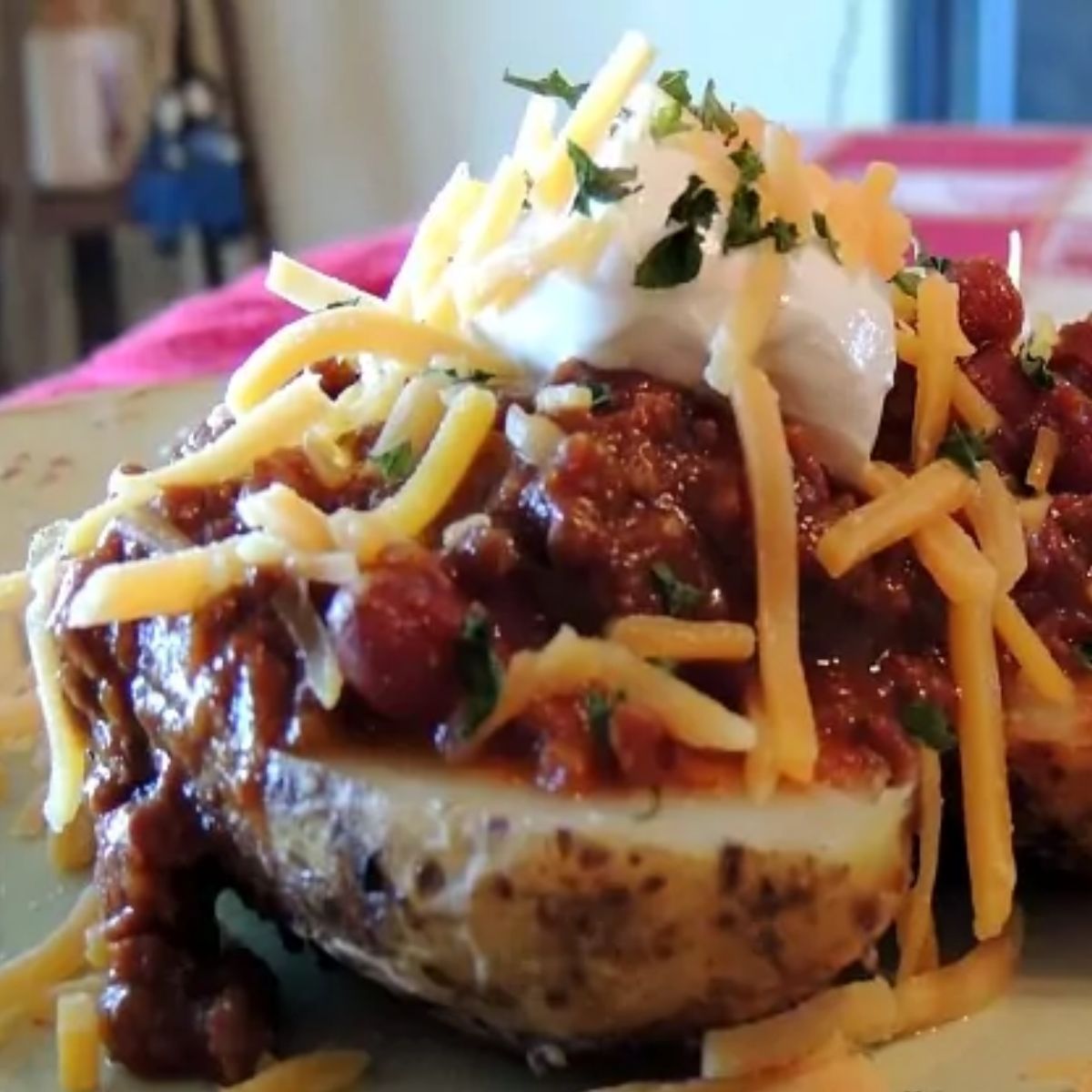 close up of chili on top of baked potato with cheese and sour cream.
