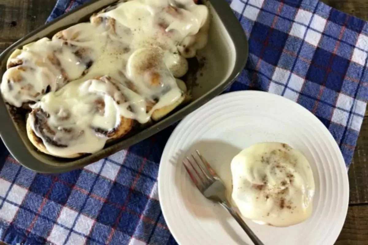 cinnamon rolls in baking dish and one served on white plate with fork.