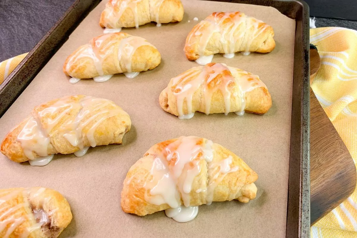 crescent rolls filled with cinnamon cream cheese on baking tray with yellow dish towel.