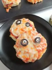 closeup of mini pizzas on black plate for Halloween.