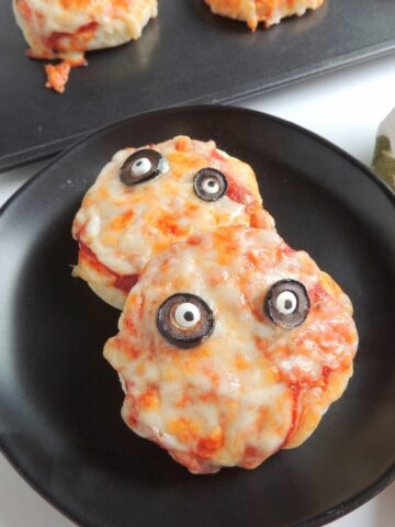 closeup of mini pizzas on black plate for Halloween.