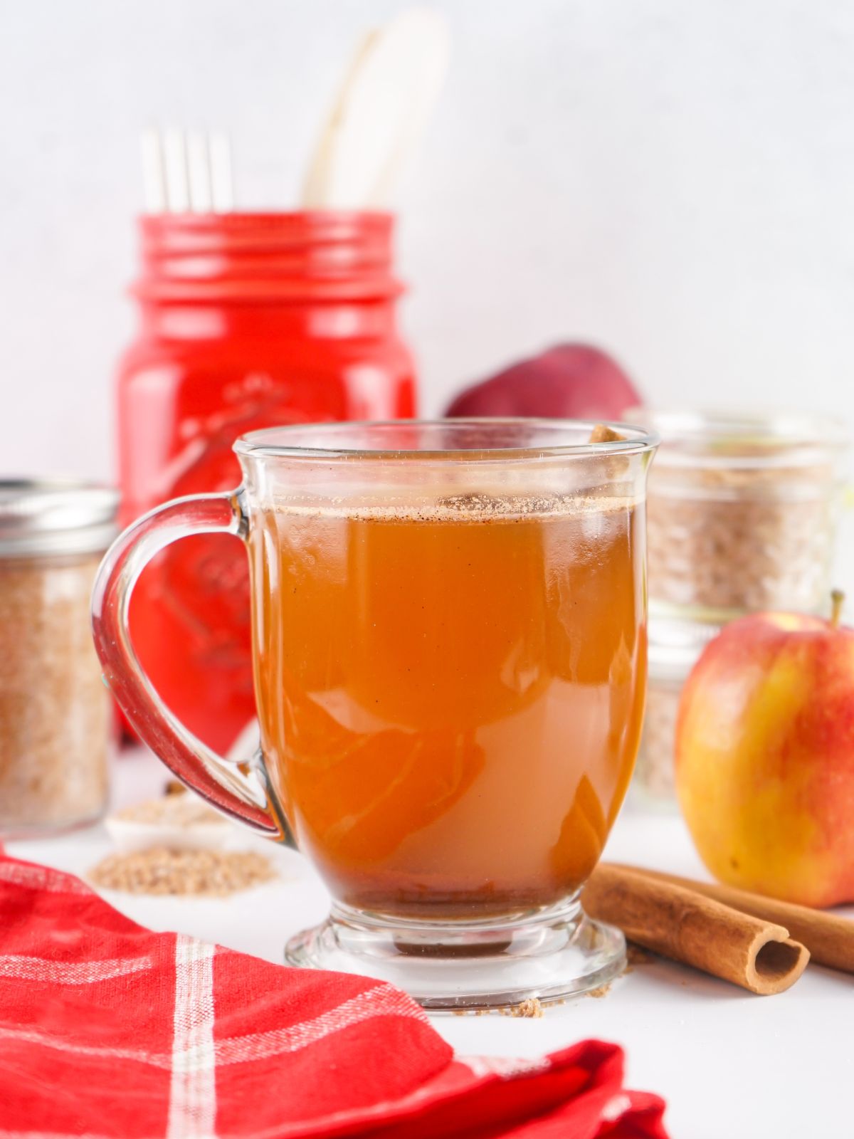 side view of apple cider in glass mug with red towel and apples.