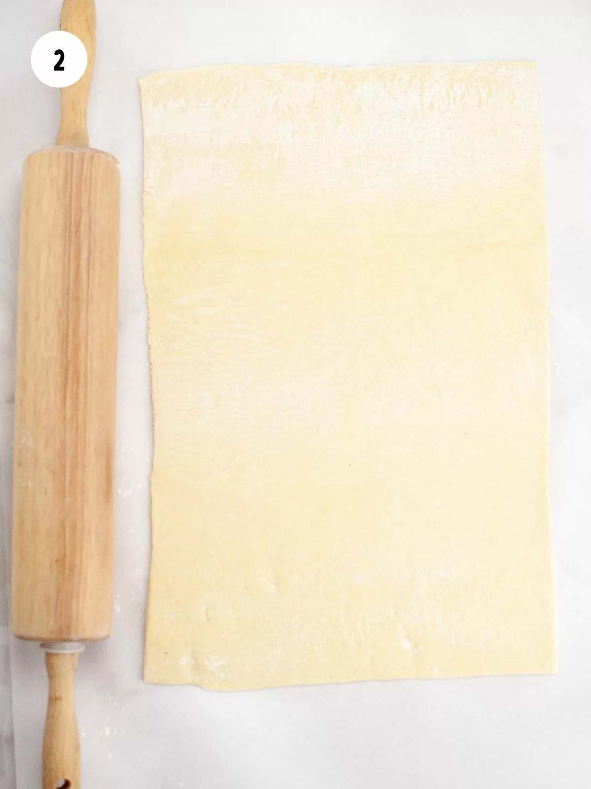 rolled out sheet of puff pastry and a wooden rolling pin to the left of it