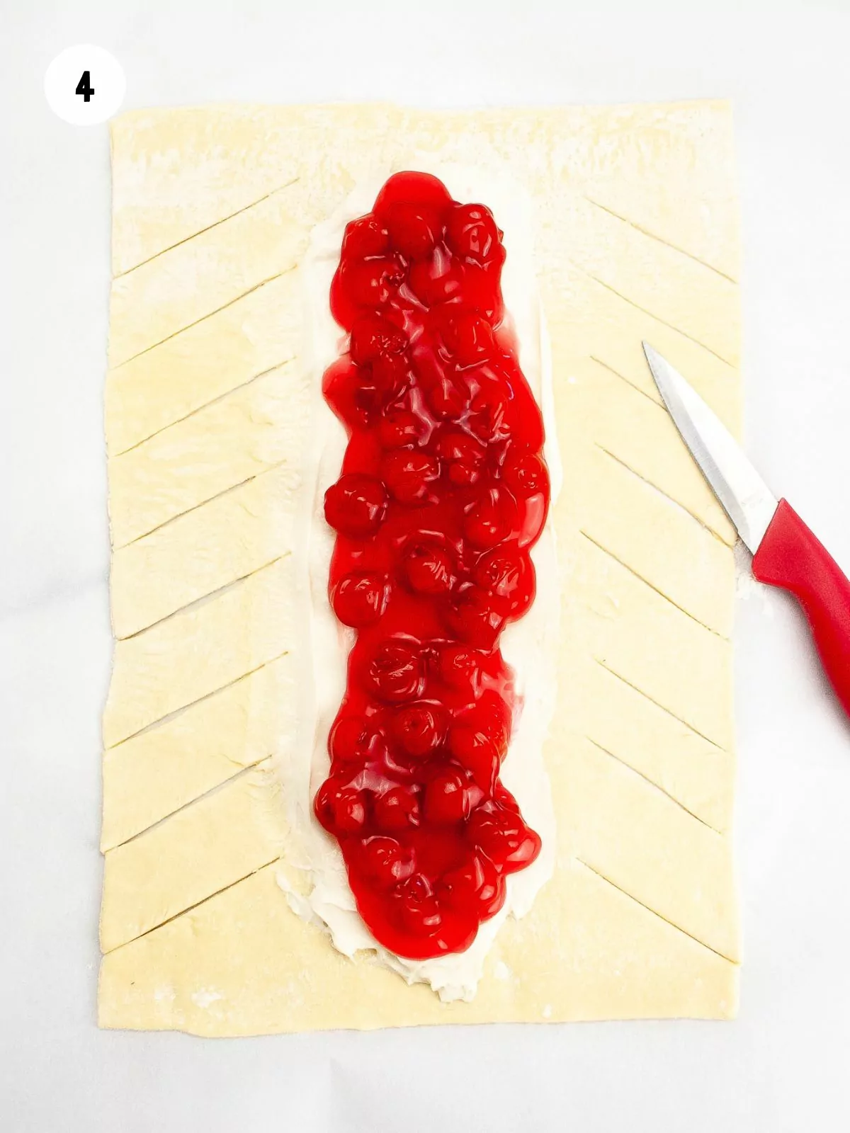 Cherry pie filling added on top of the cream cheese. Diagonal slits are cut into the sides of the puff pastry