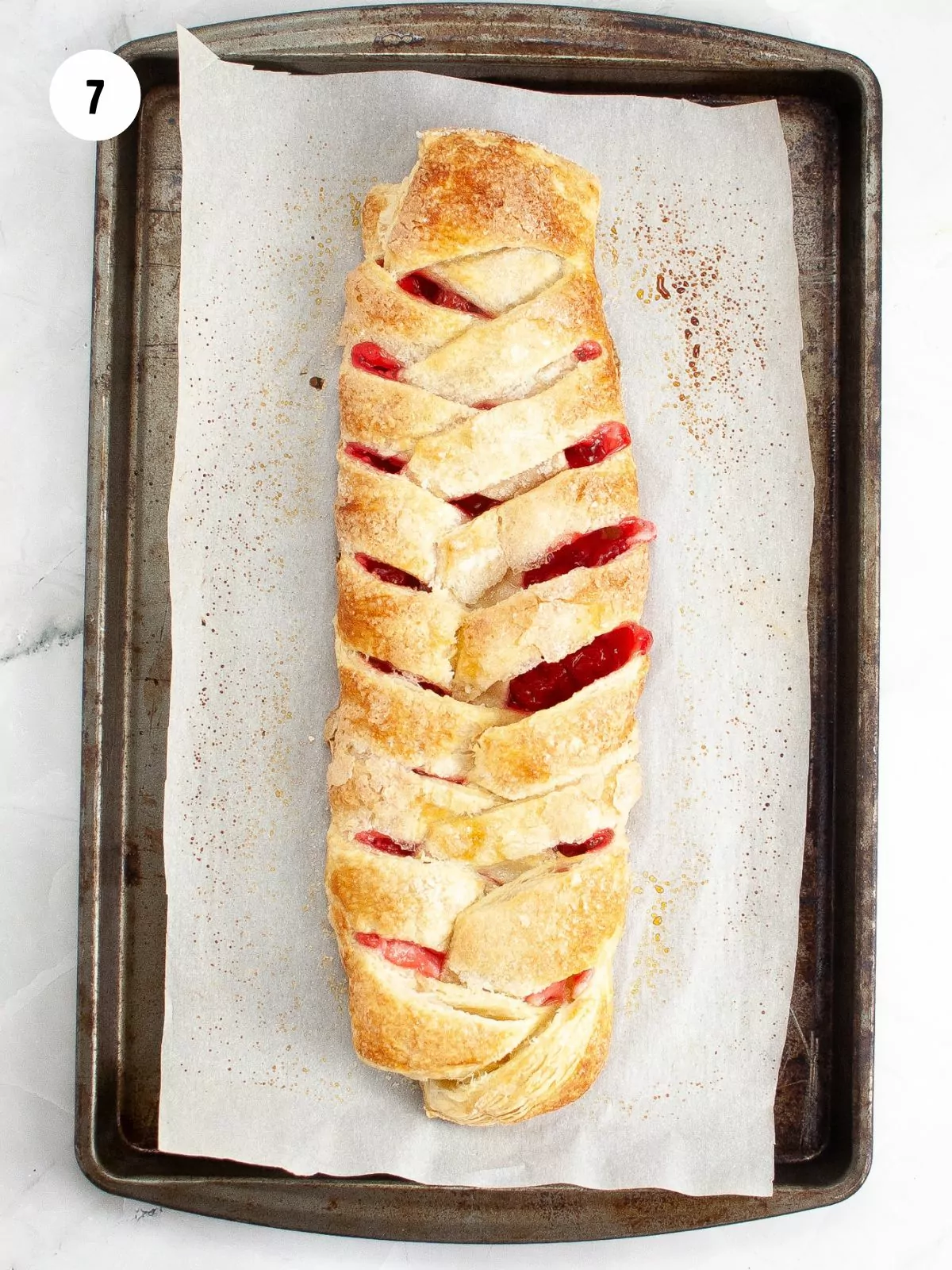 baked braided puff pastry danish with cherries on a baking sheet